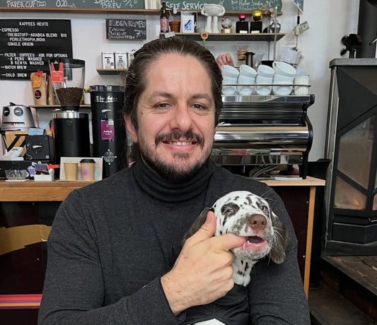 Amichai holding his puppy while sitting in a coffee shop, smiling as he cuddles the small dog in a relaxed café setting.